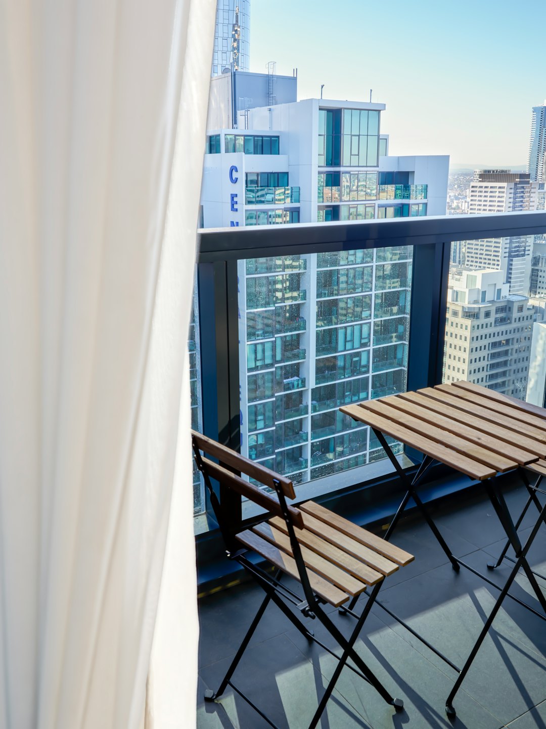 Two wooden chairs and a table on a high-rise balcony.