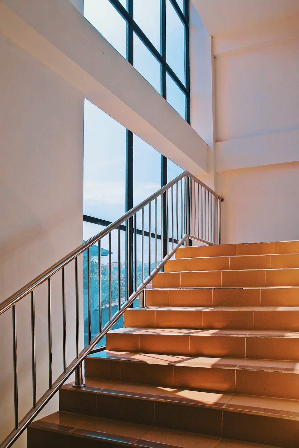 Modern staircase with a chrome railing near large windows.